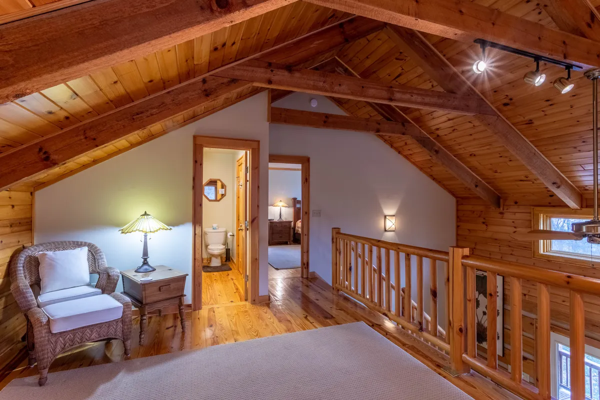 A cozy reading nook with a wicker chair, plush cushion, table lamp, and a wooden railing. The setup is intimate and perfect for quiet moments of reflection or reading, tucked away from the main living areas.