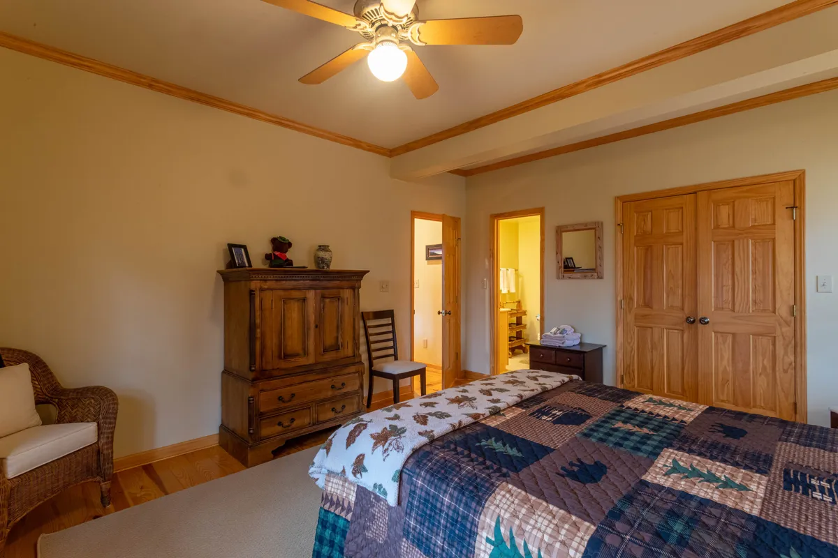 A serene bedroom with a bed covered in a quilt, a wooden dresser, and a comfortable chair placed in the corner. The lighting is soft, inviting, and suggests a calm, communal atmosphere ideal for relaxing or gathering for intimate conversations.
