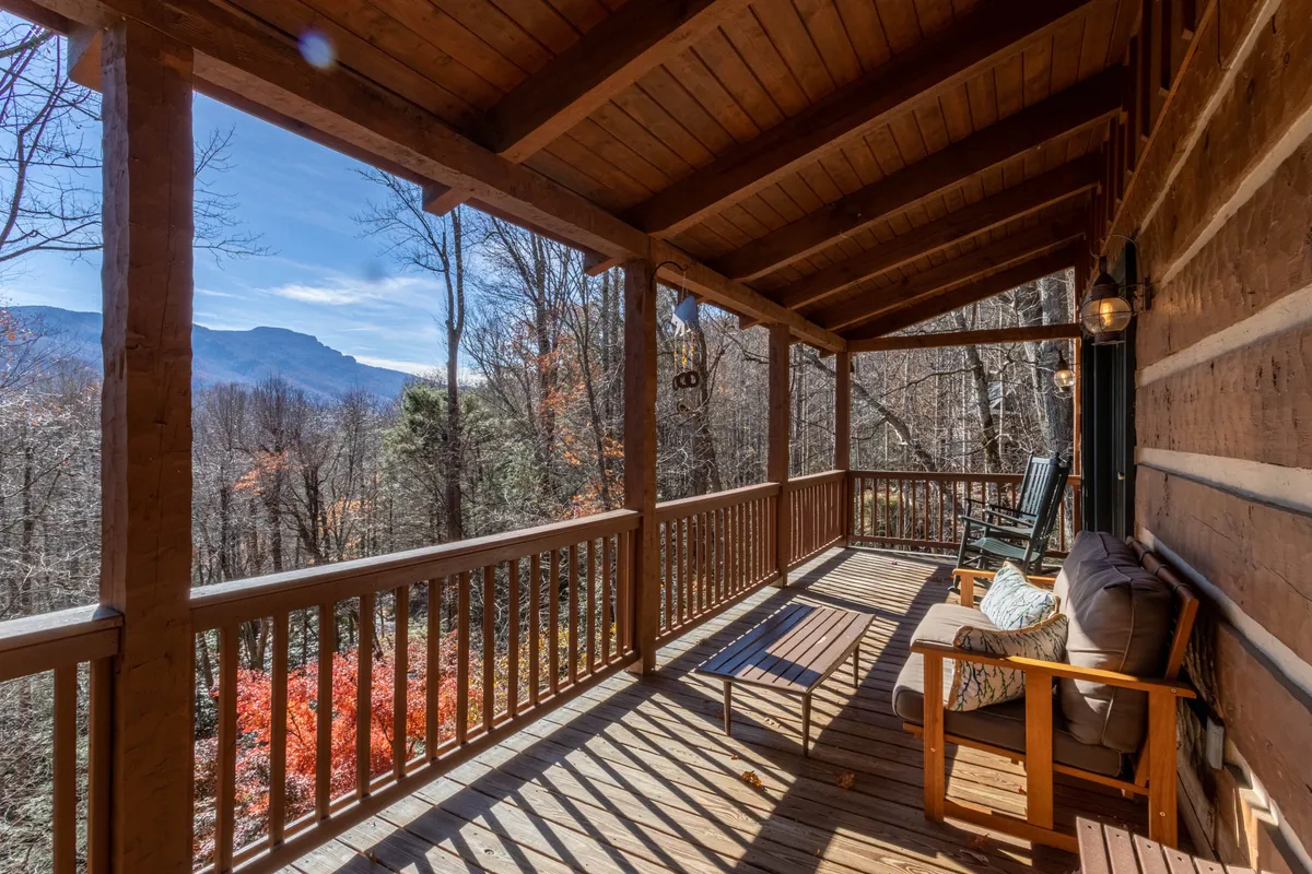 This image showcases a wooden deck outfitted with classic rocking chairs, a rustic coffee table, and sturdy wooden railings. The deck opens to a breathtaking view of the mountains, with natural surroundings visible through the open spaces. The atmosphere is peaceful and warmly inviting, perfect for enjoying sunrise coffee or sunset drinks as described in the section.