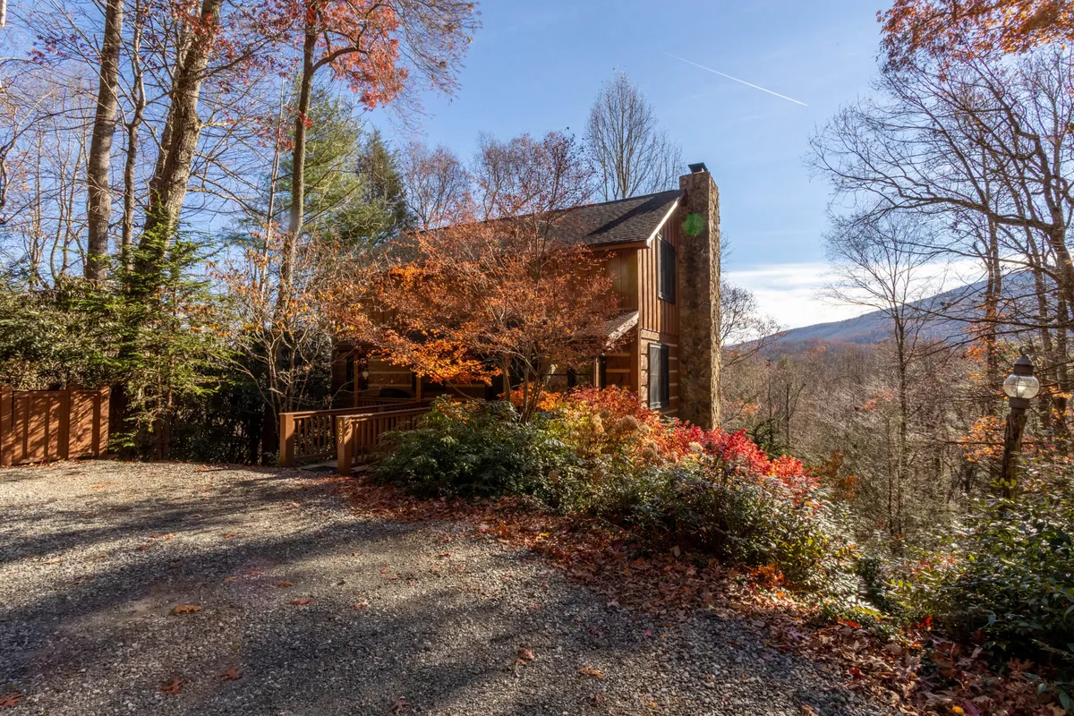 A welcoming exterior shot of the property set against vibrant autumn foliage. The wooden facade and large stone chimney evoke rustic mountain charm, while the natural surroundings hint at privacy and peace. The image captures the sense of seclusion and scenic beauty that define the retreat.
