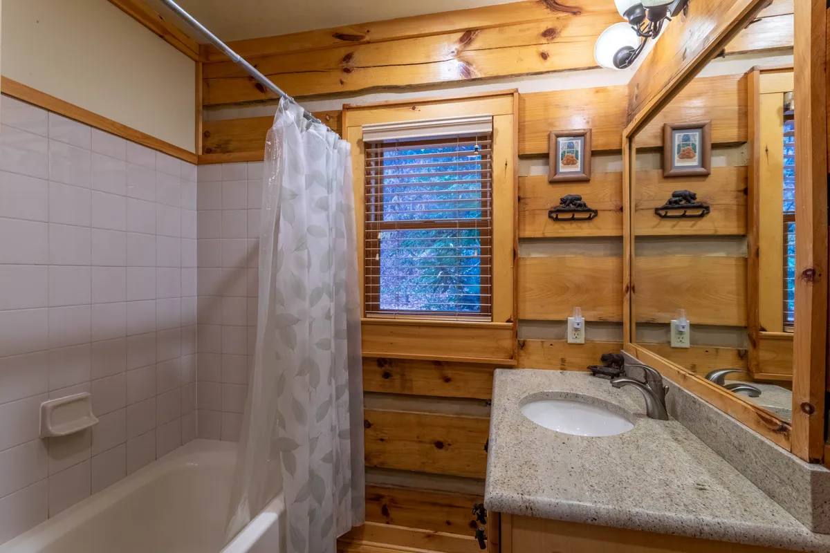 A warm bathroom scene featuring a granite countertop, wooden paneling, a large mirror, and a shower curtain. Gentle natural light streams in, creating an inviting atmosphere for self-care and relaxation.