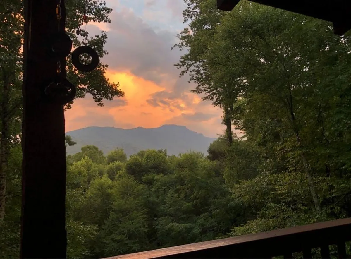 A wide-angle view captures mountains at sunset, the sky streaked with warm hues above a tranquil, wooded landscape. The scene suggests quiet reflection, photography opportunities, and peaceful evenings spent soaking in the grandeur of Grandfather Mountain.